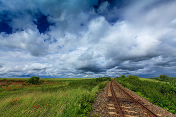 Fototapeta na wymiar Old railroad in remoter rural area in Europe on a summer day, under a sky covered with storm clouds
