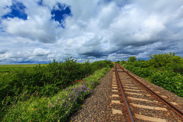 Fototapeta premium Old railroad in remoter rural area in Europe on a summer day, under a sky covered with storm clouds