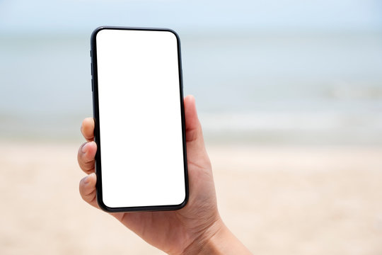 Mockup image of a hand holding and showing a black mobile phone with blank desktop screen by the sea