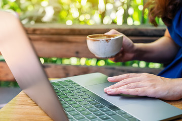 Closeup image of a woman using and touching on laptop touchpad while drinking coffee