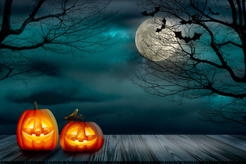 Halloween backdrop with lighting of Jack-o-lantern on the old grunge plank wood board and the silhouette trees with full moon and flying bats on the mystery dark cloud at night.