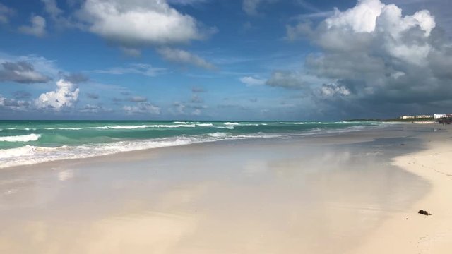 Slow motion camera pan along caribbean white sandy beach with cloud formations