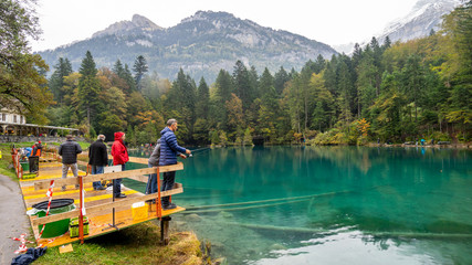 Blausee, Switzerland - October 13, 2016: People and tourist fishing for trout on rainy day with colorful autumn leaves, blue water in Kandergrund, Switzerland