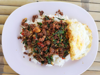 Stir fried basil with minced meat. Served with fried egg and on top of rice. Popular Thai street food. Top view on table.
