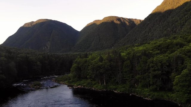 Drone shot rising up over a river, 3 mountains in background.