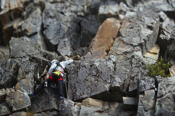 Figure of the girl climber on a difficult rocky relief, back view. Tilt-Shift effect. Climbing gear. Climbing equipment.