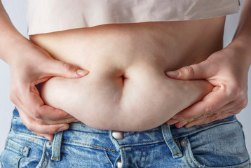 Woman's hand holding excessive belly fat on blue background, the concept of weight loss	