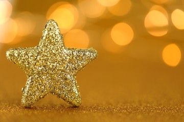 Christmas festive background.Gold glitter star on a gold  background with yellow shining bokeh.Christmas and New Year background. Winter holidays wallpaper. Golden shiny wallpaper.