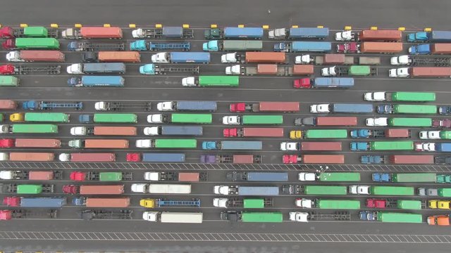 AERIAL, TOP DOWN: Couple of trucks get to drive past the long line waiting in the busy harbor. Flying above a few loaded cargo trucks driving past a queue of others waiting in the Port of Los Angeles.