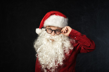Portrait of a boy in the image of Santa Claus on a dark background .