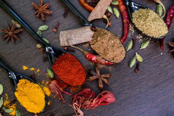 Set of Various spices decorated on spoon on a dark wooden table. Chilly pepper, rosemary, basil,...