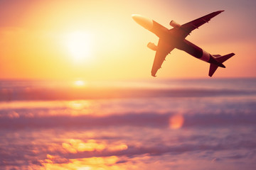 Airplane flying over tropical beach with smooth wave and sunset sky abstract background.