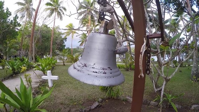 A female person ringing a large bell near an island cemetery