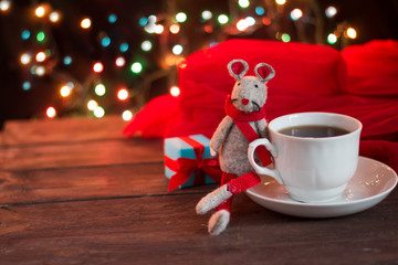 Obraz na płótnie Canvas Christmas coffee on a dark wooden table. Blurred garland lights in the background. Freshly brewed coffee in a white cup. Good New Year spirit. Symbol of the year 2020 toy rat.