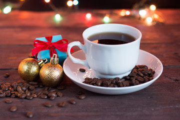 Christmas coffee on a dark wooden table. Blurred garland lights in the background. Freshly brewed coffee in a white cup. Good New Year spirit.
