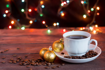 Christmas coffee on a dark wooden table. Blurred garland lights in the background. Freshly brewed coffee in a white cup. Good New Year spirit.
