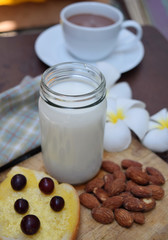 Healthy breakfast consists of milk in a white glass. Butter bread with black grapes, almonds and black coffee in a white glass