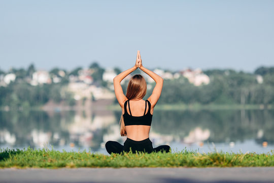 Woman sitting in meditation pose outdoor with hands up in namaste. Back view- Image