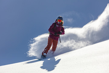 Freeride snowboarder girl riding off-trail fresh powder snow high in the mountains. Unrecognizable woman heliski snowboarding untouched terrain in snowy mountains. Heliboarding remote pristine slopes