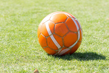 An old rugged used orange soccer ball or football on the ground of grass. 