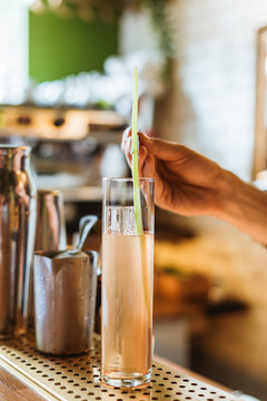Putting a garnish into a highball cocktail glass with a drink. Lifestyle vertical image. Selective focus.