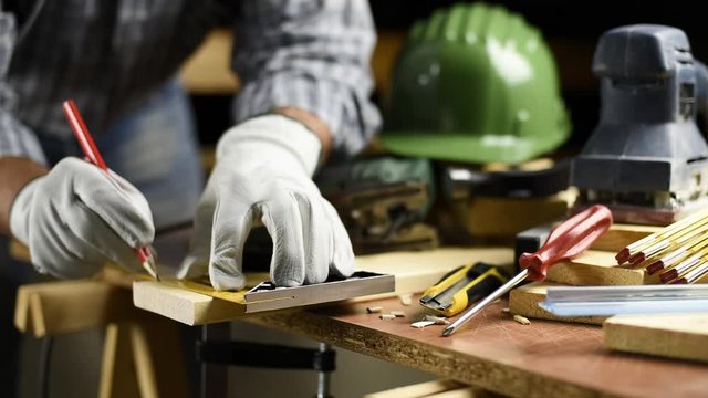 Adult carpenter craftsman wears protective leather gloves, with a pencil and the carpenter's square trace the cutting line on a wooden table. Construction industry, housework do it yourself. Footage.