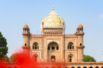 (Selective focus) Stunning view of the Safdarjung Tomb in the background and blurred red Hibiscus flowers in the foreground. New Delhi, India.