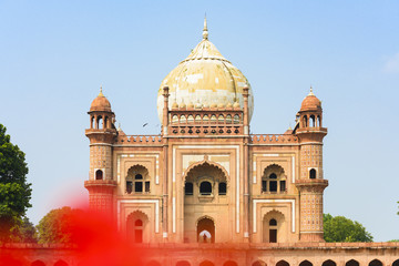 Fototapeta na wymiar (Selective focus) Stunning view of the Safdarjung Tomb in the background and blurred red Hibiscus flowers in the foreground. New Delhi, India.