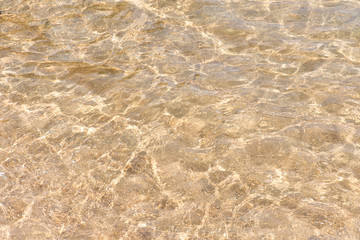 Fototapeta na wymiar Water rippled and sunny reflections on the surface of gold sand in the sea.