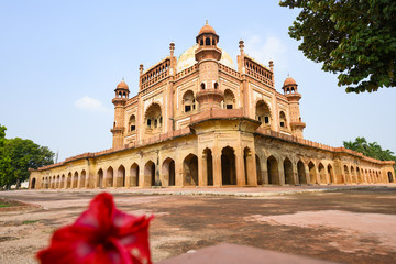 Fototapeta premium (Selective focus) Stunning view of the Safdarjung Tomb in the background and blurred red Hibiscus flowers in the foreground. New Delhi, India.