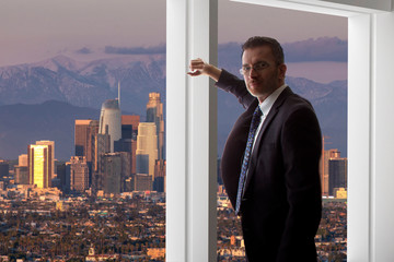 Businessman looking at the buildings of downtown Los Angeles from an office window.  The man looks...