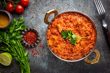 Chicken meat with tikka masala sauce, spicy curry food in iron copper pot with seasonings, top view