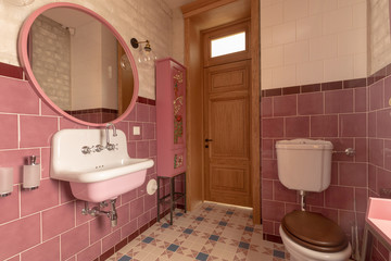 Interior of clean light restroom with retro sink beside big round mirror and decorated cabinet on...