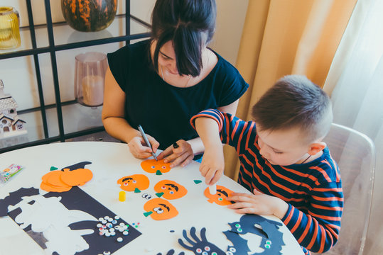 young mother with toddler son making craft pumpkins for halloween holiday