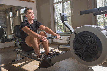 The athlete is engaged in the gym, the Young man works on the rowing simulator