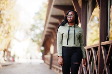 City portrait of positive young dark skinned female wearing green hoody and eyeglasses.