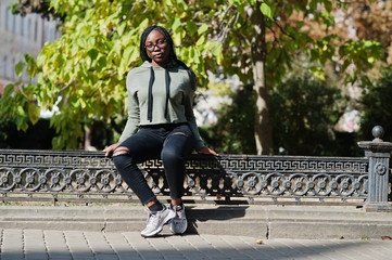 City portrait of positive young dark skinned female wearing green hoody and eyeglasses.