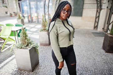 City portrait of positive young dark skinned female wearing green hoody and eyeglasses.