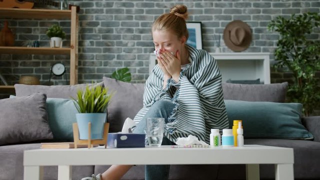 Young woman covered with blanket is coughing in paper tissue wiping nose feeling sick at home. Human health problems, treatment and lifestyle concept.
