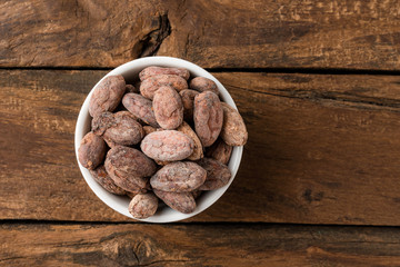Cocoa beans in bowl on rustic wooden table. Top view