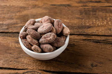 Cocoa beans in bowl on vintage wooden table