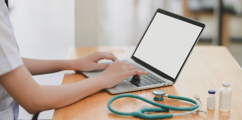 Close-up view of young female doctor examining the patient chart while using mock up laptop computer - obrazy, fototapety, plakaty