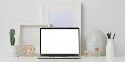 Minimal workspace with open blank screen laptop computer with mock up frames and ceramic vase decoration