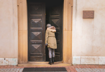 Una joven cotilla dentro de un edificio. Imagen de invierno con abrigo y sombrero dando la espalda al fot&oacute;grafo.