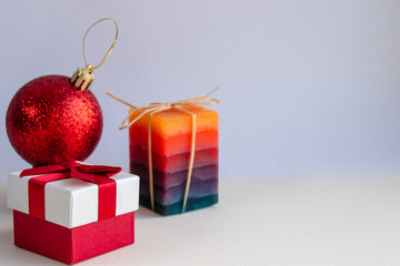 A festive composition consisting of a decorative candle, a Christmas toy and a gift box tied with a red ribbon