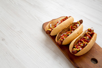 Homemade hot dogs with chicken sausage on a rustic wooden board on a white wooden background, side view. Copy space.