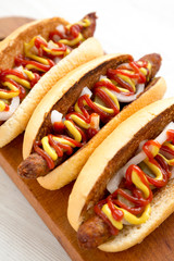 Homemade hot dogs with chicken sausage, ketchup and mustard on a rustic wooden board on a white wooden table, low angle view. Closeup.