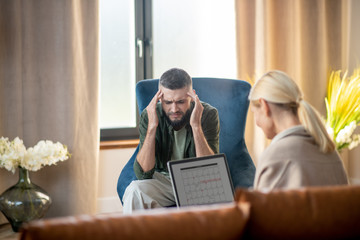 Man having headache while talking to psychologist