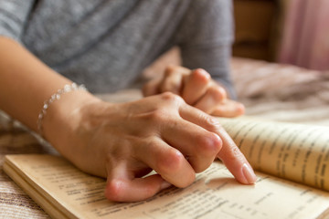 Young woman having rheumatoid is reading a book. Hands and legs are deformed. She feels pain....