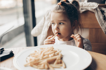 sweet girl eating favorite french fries in restaurant  